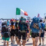 Giovani pellegrini con zaini e bandiere si dirigono verso Tor Vergata per il Giubileo 2025